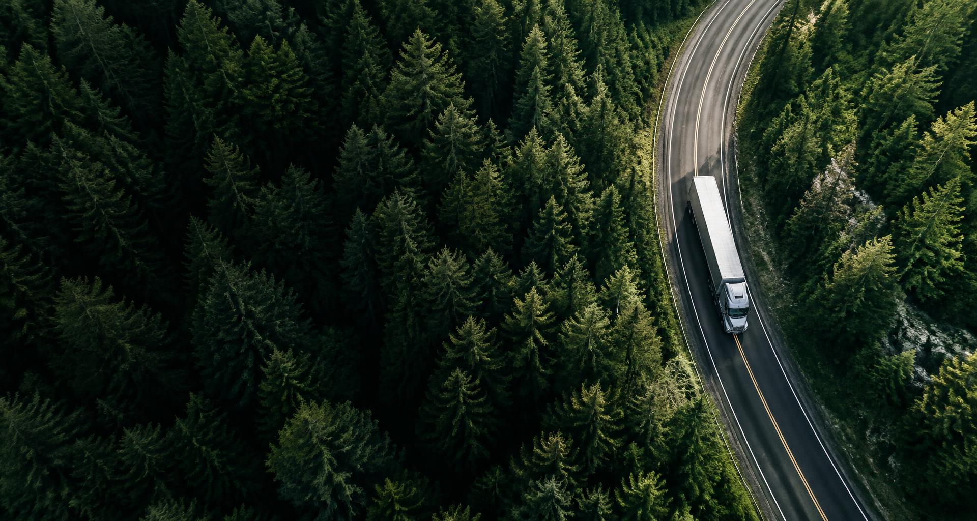 An aerial view of a freight truck moving along a forest highway